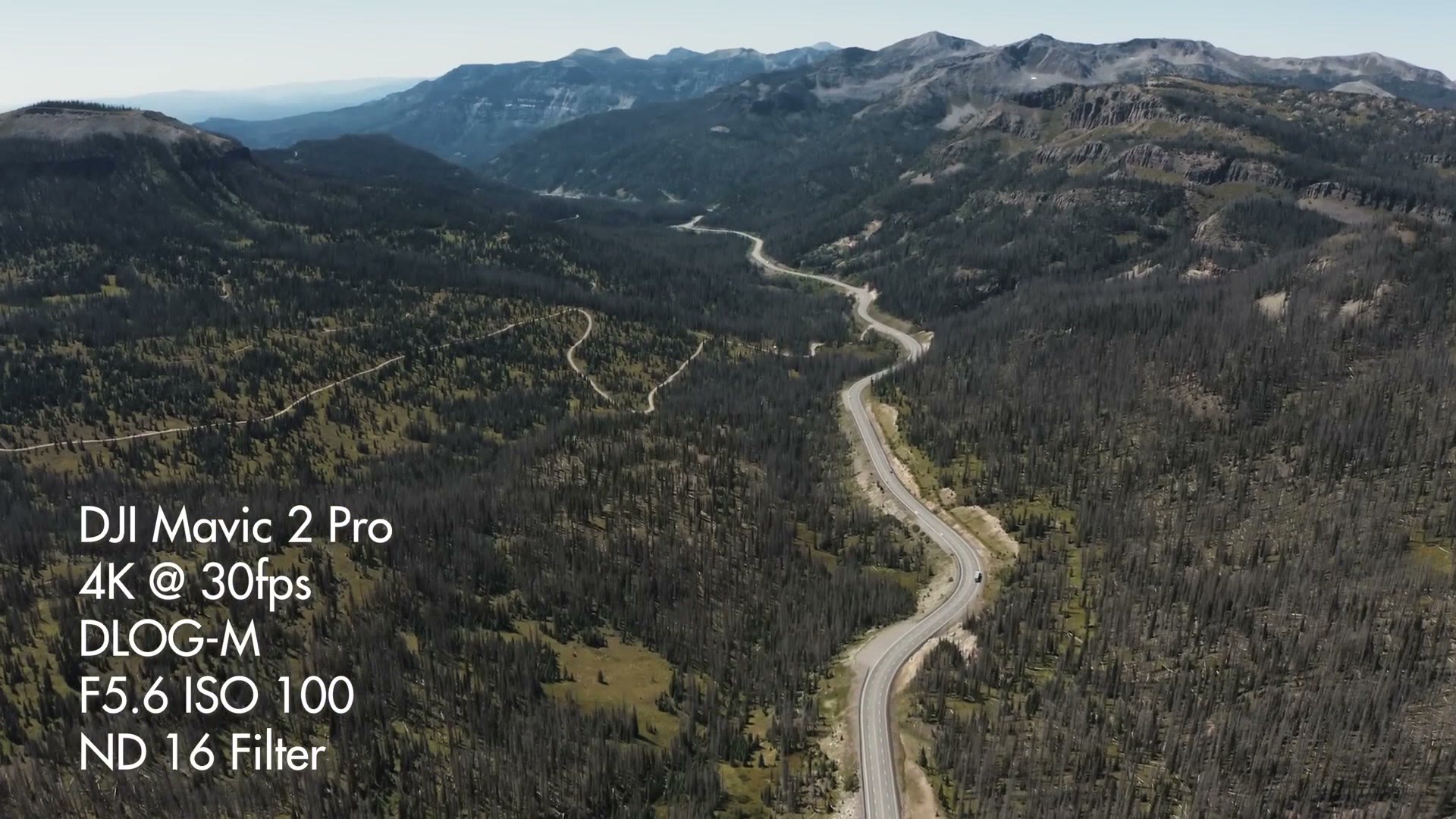 Aerial view of a road winding through a forested Colorado valley, overlaid with settings reading DJI Mavic 2 Pro, 4K at 30fps, DLOG-M, F5.6 ISO 100, ND 16 filter