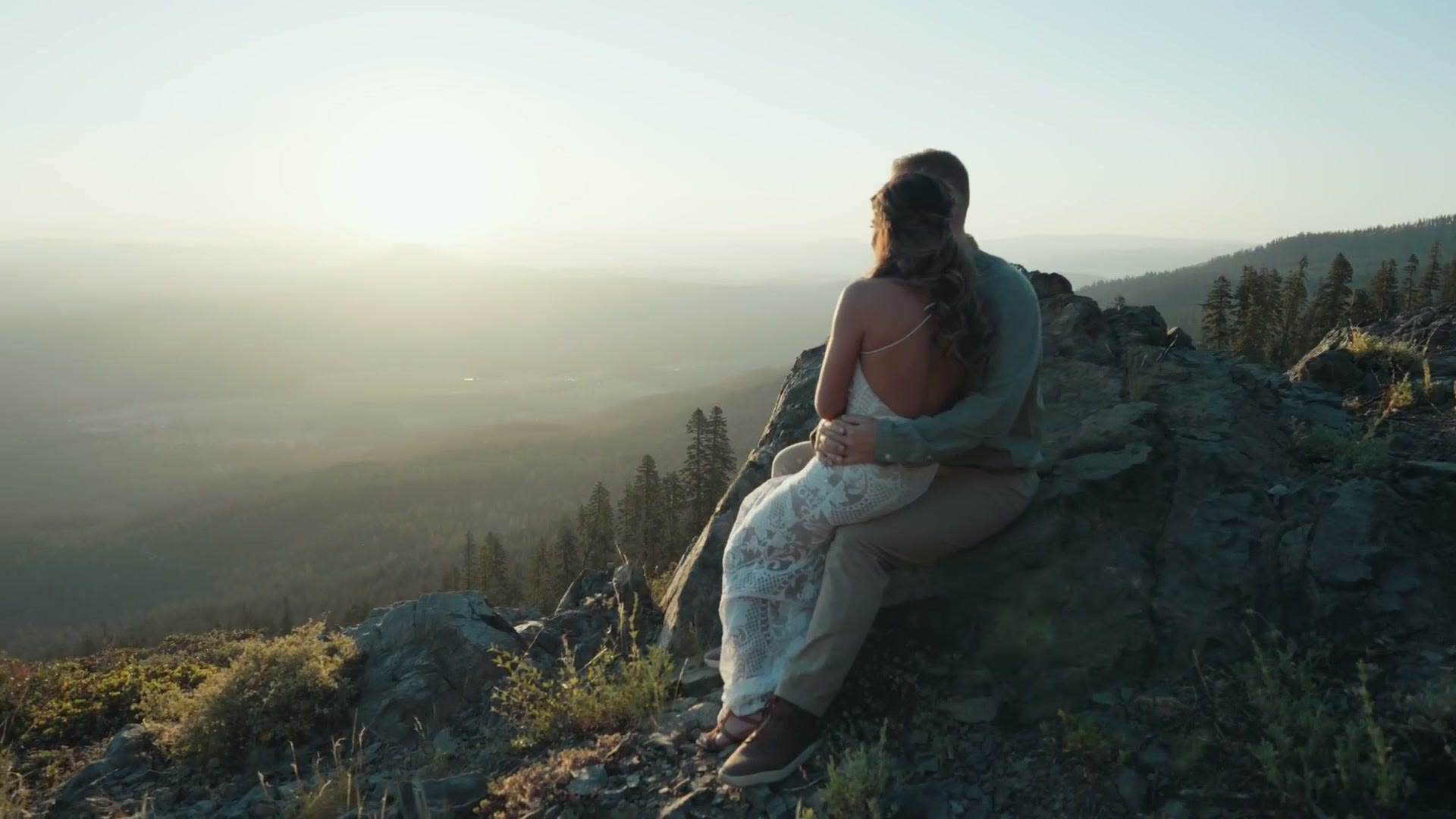 The couple sitting on a rocky outcrop at sunrise