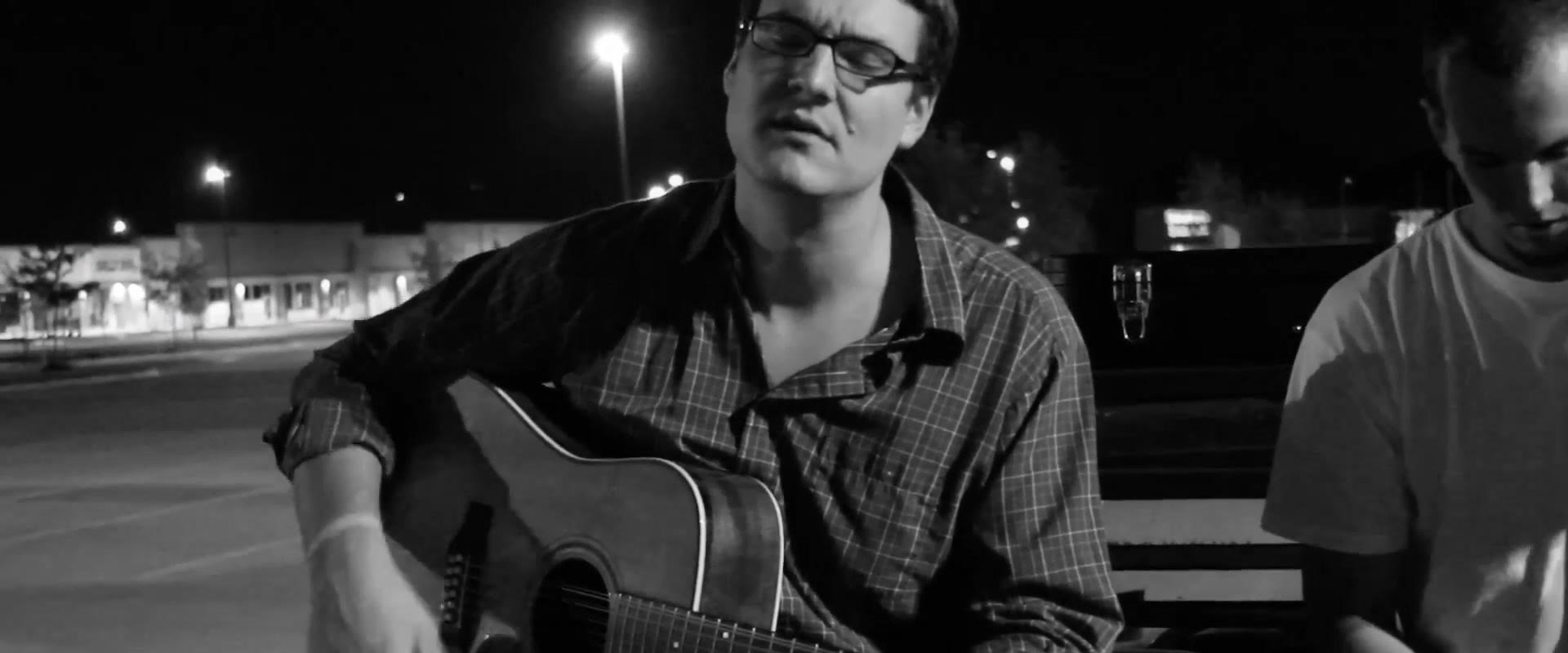 Black and white shot of Curt Vernon singing with eyes closed, another musician's arm visible seated beside him
