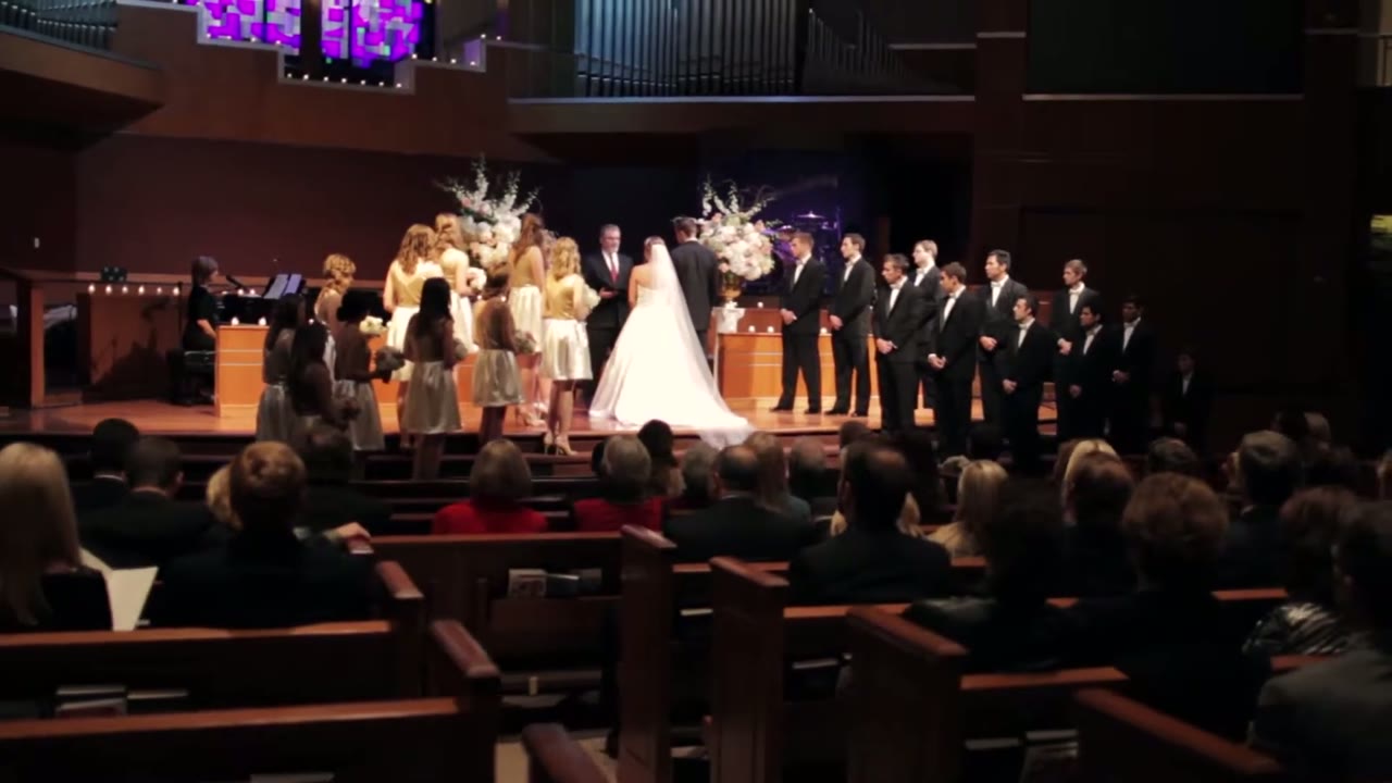 Wide view of the church sanctuary during the vows, wedding party lined up on stage below organ pipes