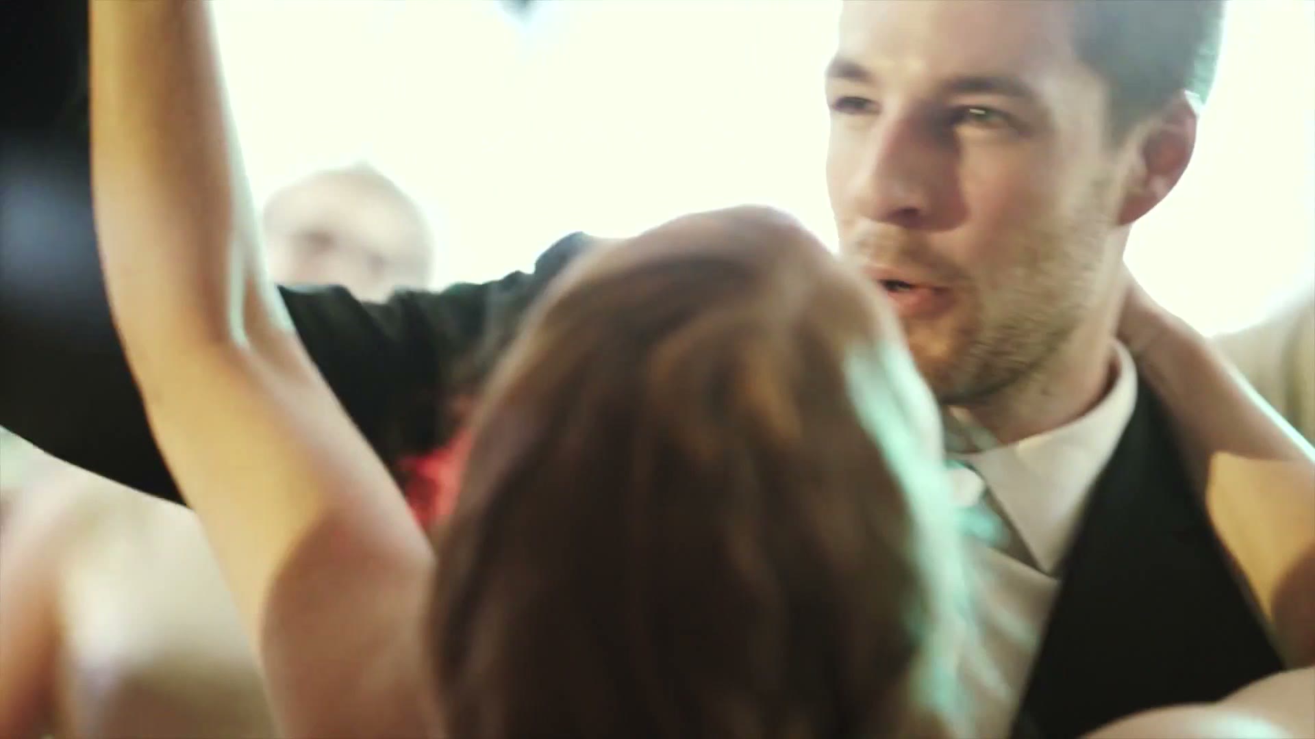 Close-up of the groom dancing at the reception, arm raised beside a woman, bright lights blown out behind them