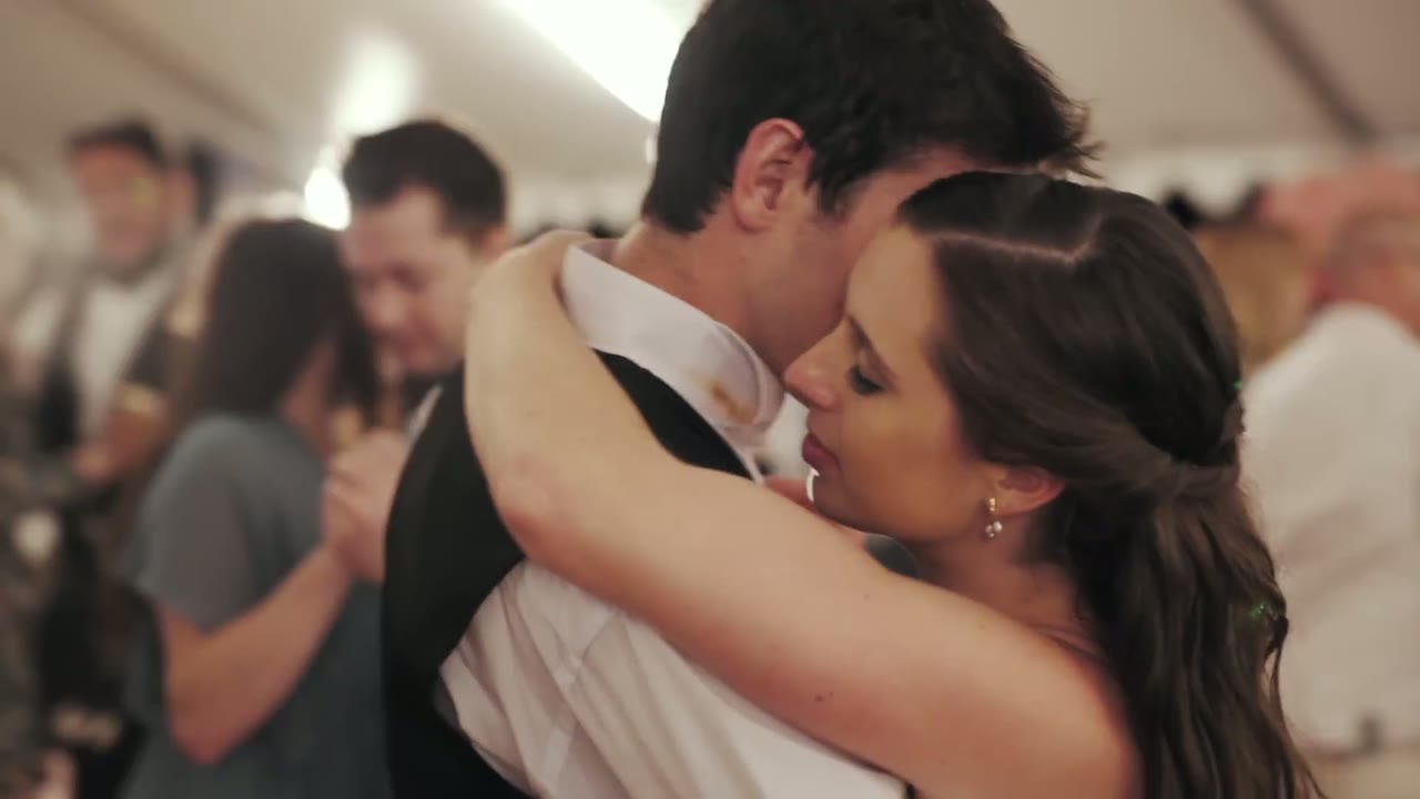 Bride and groom slow dancing cheek to cheek under the reception tent, other couples dancing behind them