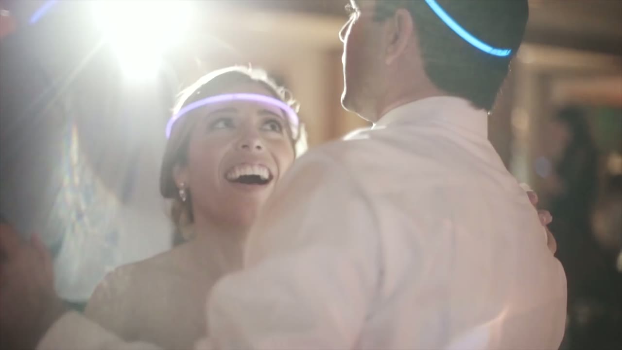 Bride laughing up at the groom while dancing, both wearing glow-in-the-dark headbands lit purple and blue