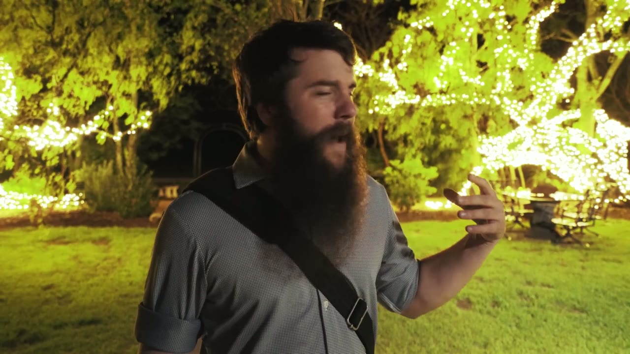Matt talking to camera at night, string lights glowing green through the trees behind him