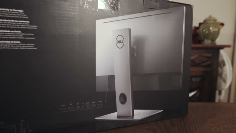 A Dell 4K monitor still half inside its box on a desk, showing the thin bezel and the stand