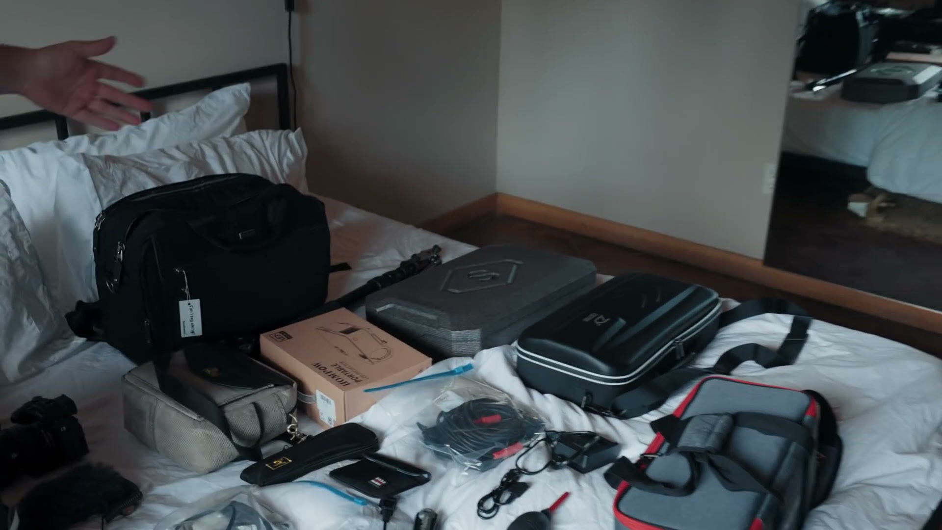 A hotel bed covered end to end with camera bags, hard cases, tripod bags, cables and lighting cases.