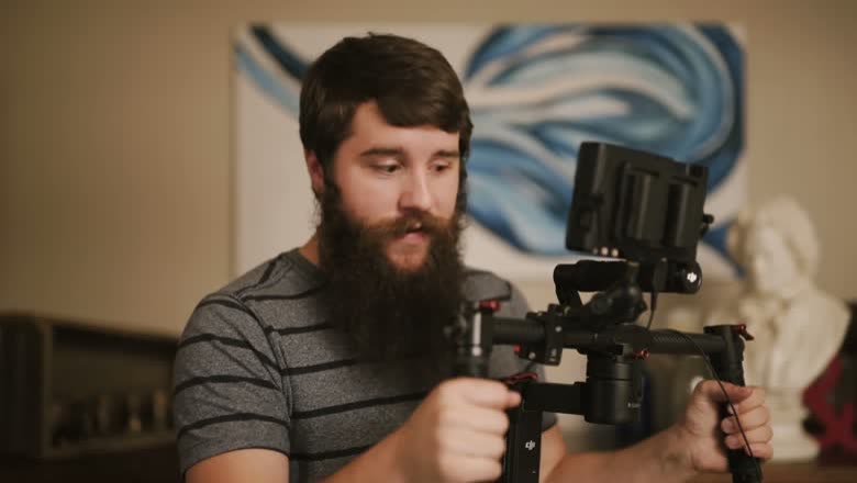 Holding the DJI Ronin-M by its two handles with a camera and external monitor mounted on the gimbal