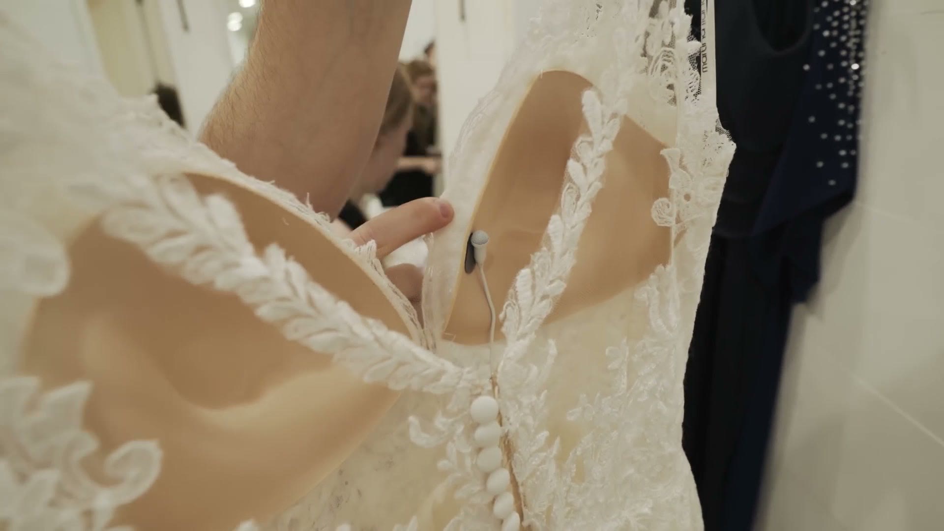 Close-up of a white lavalier microphone and cable hidden against the lace back of a wedding dress.