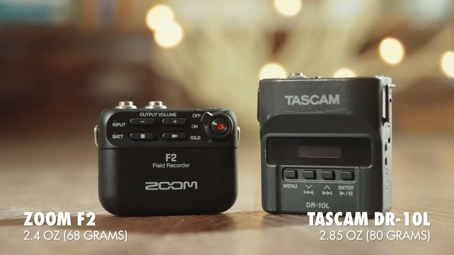 A Zoom F2 and a Tascam DR-10L standing side by side on a wooden table, labelled Zoom F2 2.4 oz (68 grams) and Tascam DR-10L 2.85 oz (80 grams).