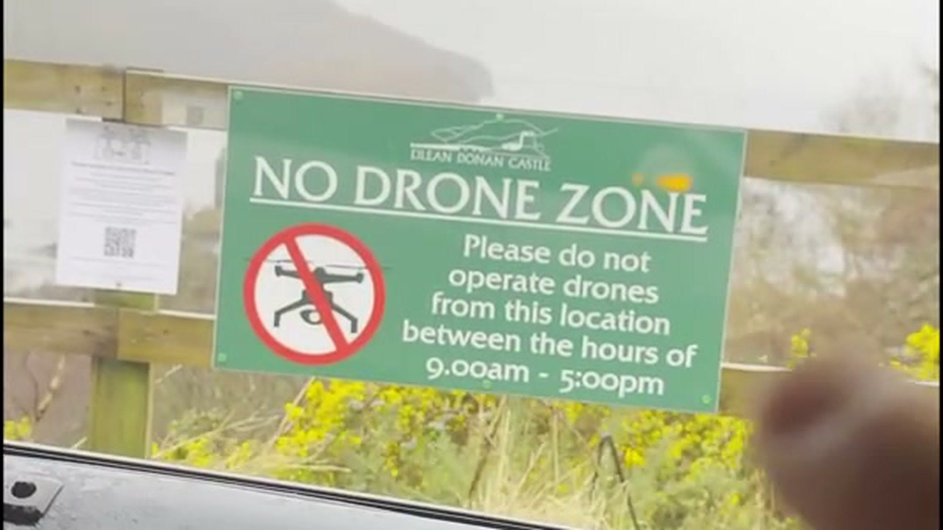 A green sign at Eilean Donan Castle reading NO DRONE ZONE, please do not operate drones from this location between the hours of 9.00am and 5.00pm