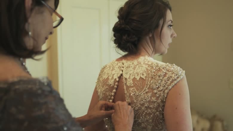 The bride's mother buttoning the long row of covered buttons up the back of her beaded lace gown