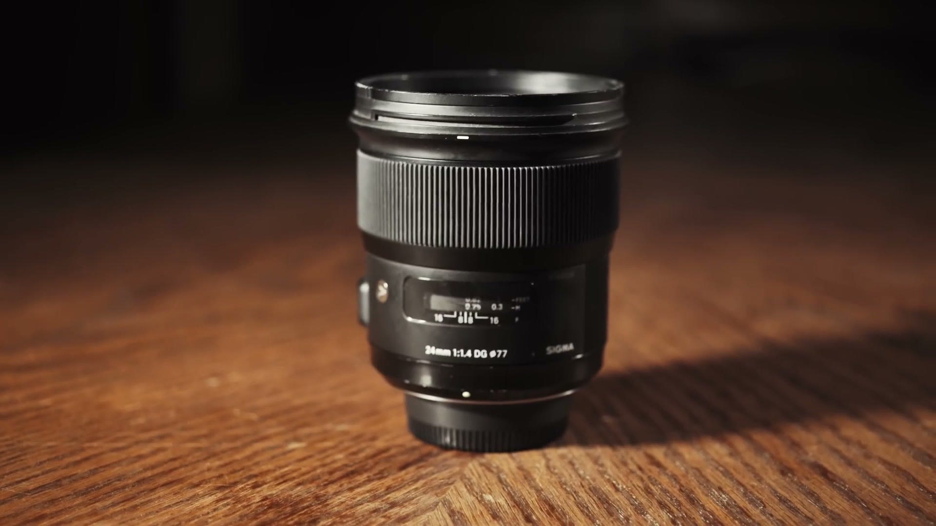 A Sigma 24mm f1.4 DG lens standing on a wooden table in warm low light