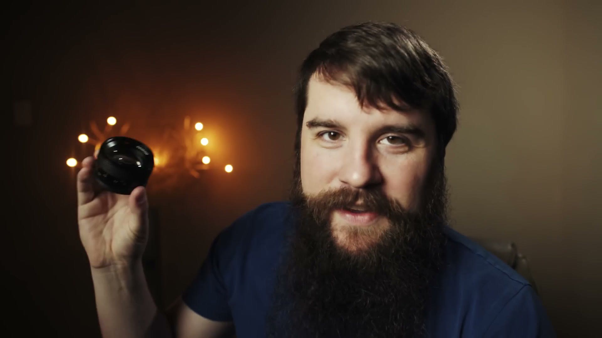 Matt holding up a very small Contax Zeiss 50mm lens beside his head, dwarfed by his beard
