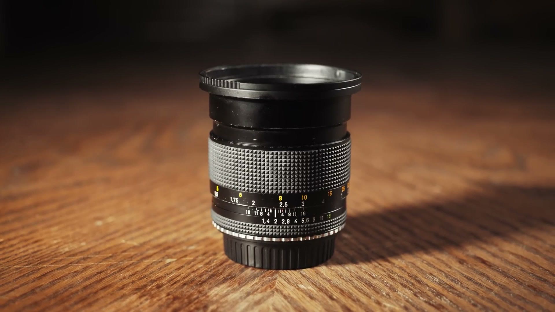 A Contax Zeiss Planar 85mm f1.4 lens standing on a wooden table, showing its knurled focus ring and aperture scale