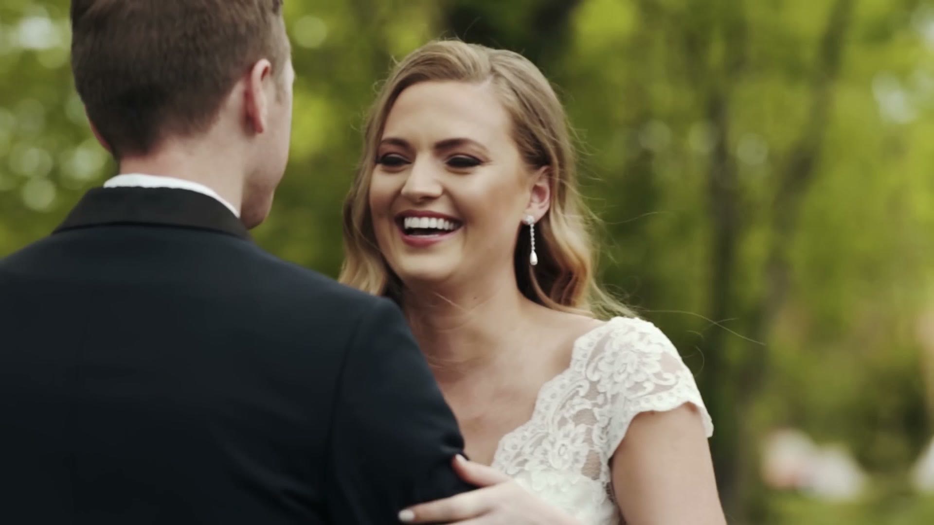 A wedding couple laughing together outdoors, filmed tight on a long lens with a soft green background