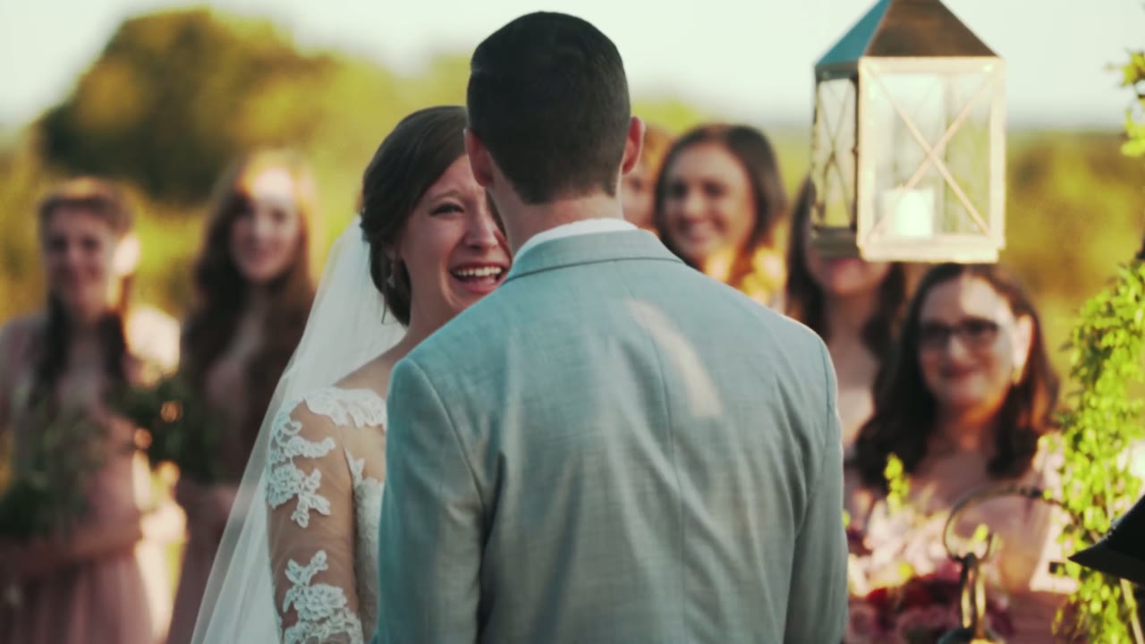 Bride laughing with the groom's back to camera, bridesmaids smiling behind her, a lantern hanging beside them
