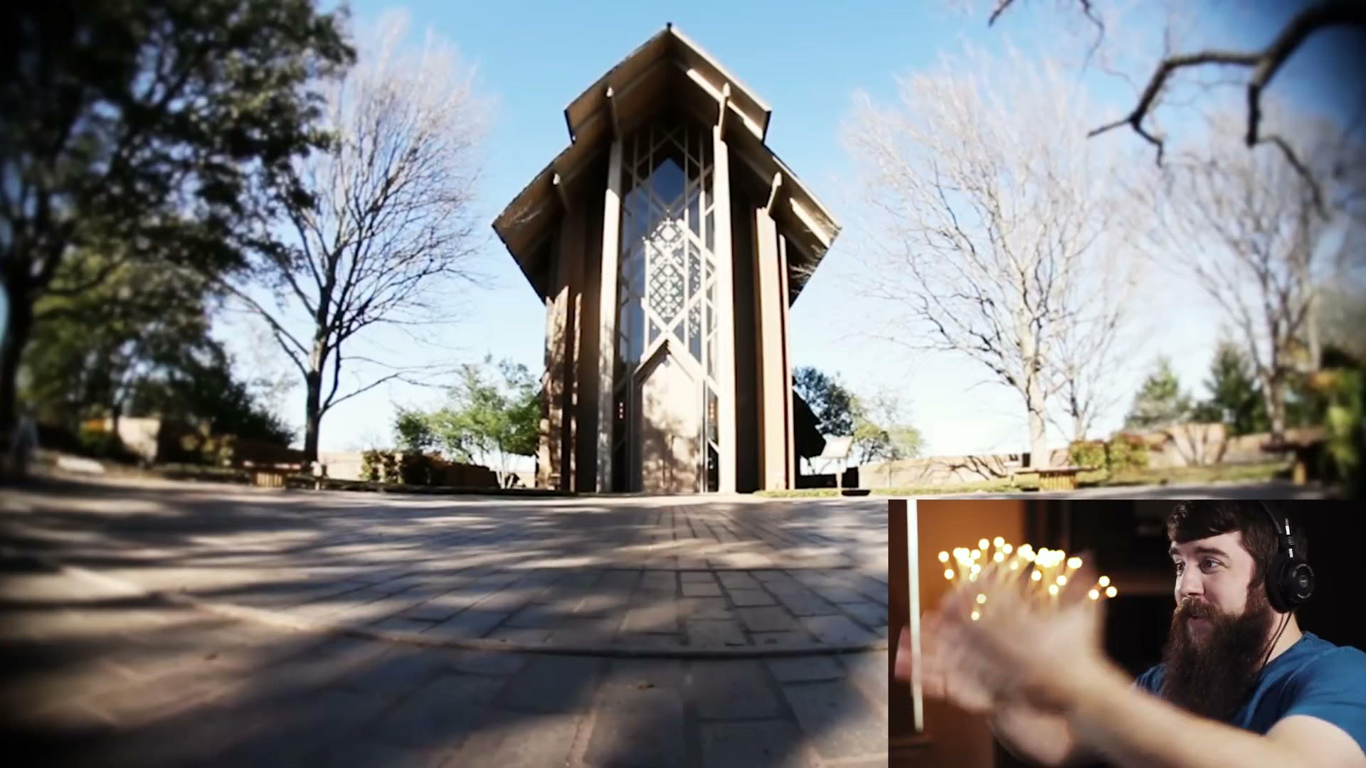 A fisheye shot of a tall glass and timber chapel with heavily bowed edges and a dark vignette, with Matt reacting in a small inset in the corner.
