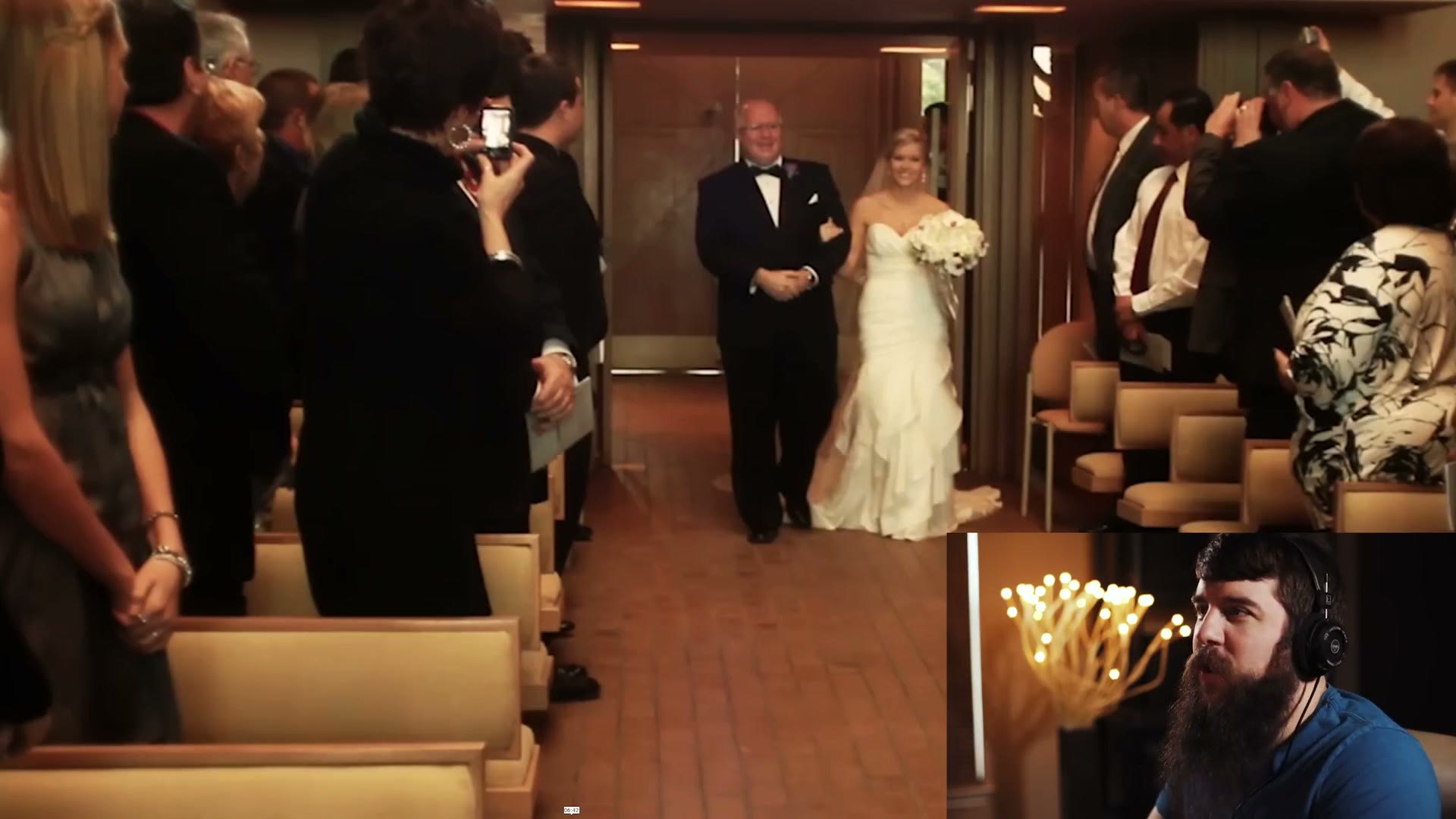 A bride walking down the aisle on her father's arm while a guest in the foreground holds up a compact point and shoot camera.