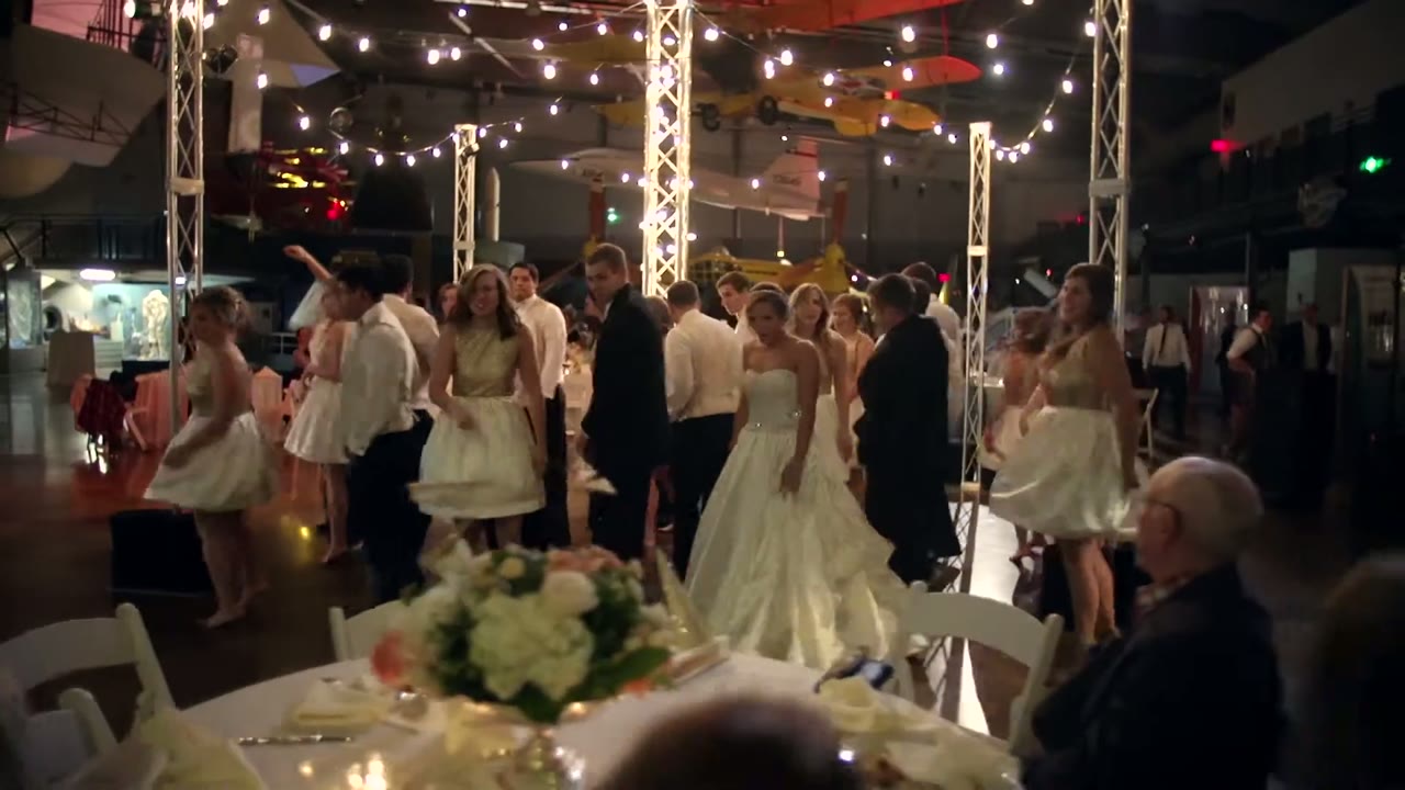 Reception dance floor at the Frontiers of Flight Museum, guests dancing under string lights with a vintage plane overhead