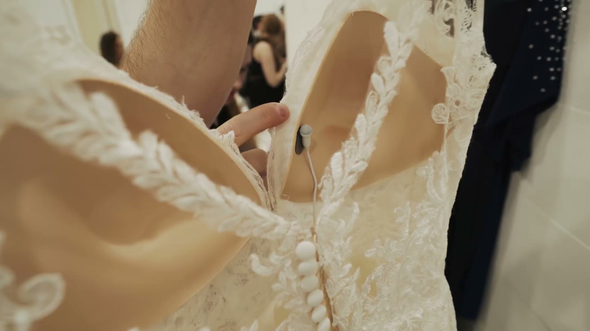 A lavalier microphone tucked inside the bodice of a white lace wedding dress on a hanger