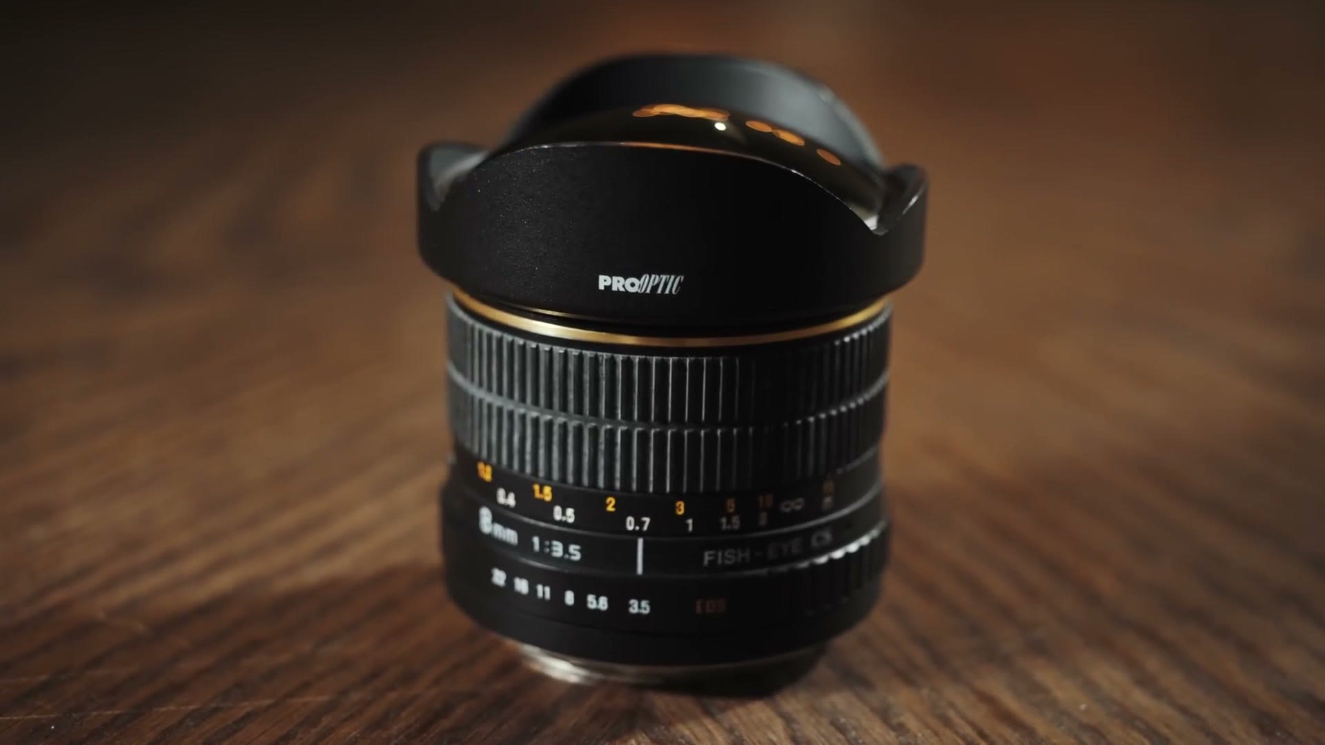 A Pro Optic 8mm f3.5 fisheye lens with a petal hood standing on a wood table