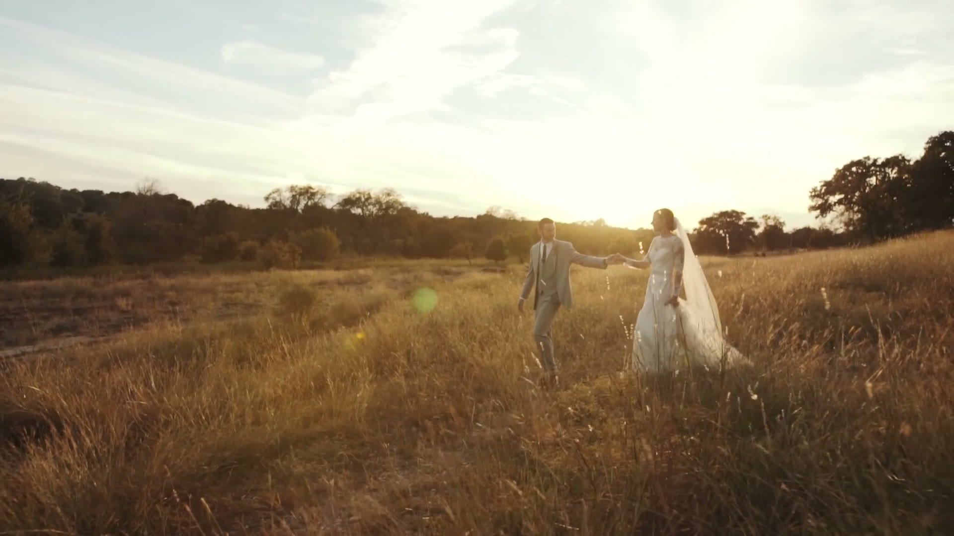A wedding couple holding hands walking through a tall golden field at sunset
