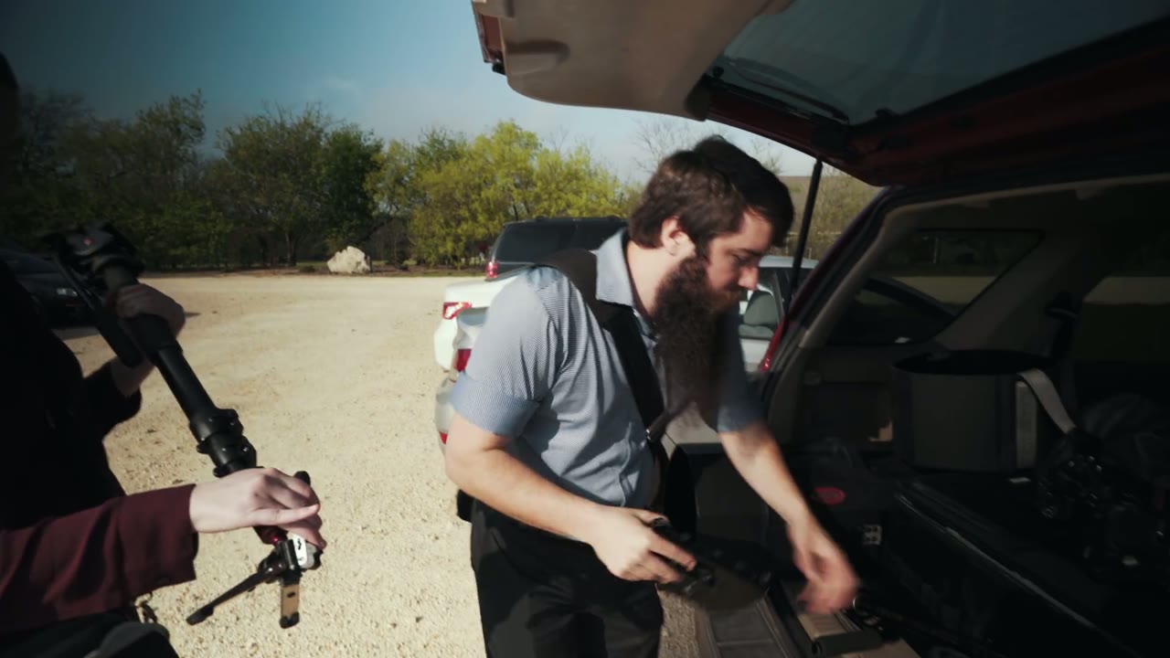 Matt unloading a glidecam and monopod case from the trunk as a second camera operator films from the foreground
