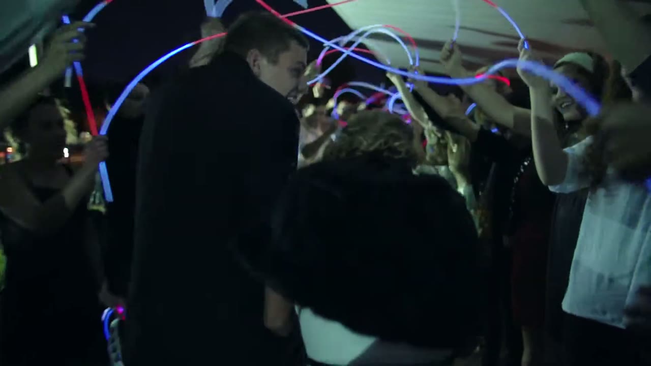 Newlyweds walking through a tunnel of glow sticks held up by guests at night