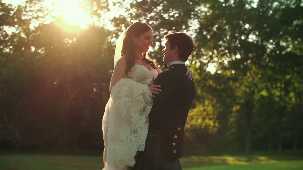 Bride and groom embracing in golden hour light, his kilt visible below her lace-trimmed veil