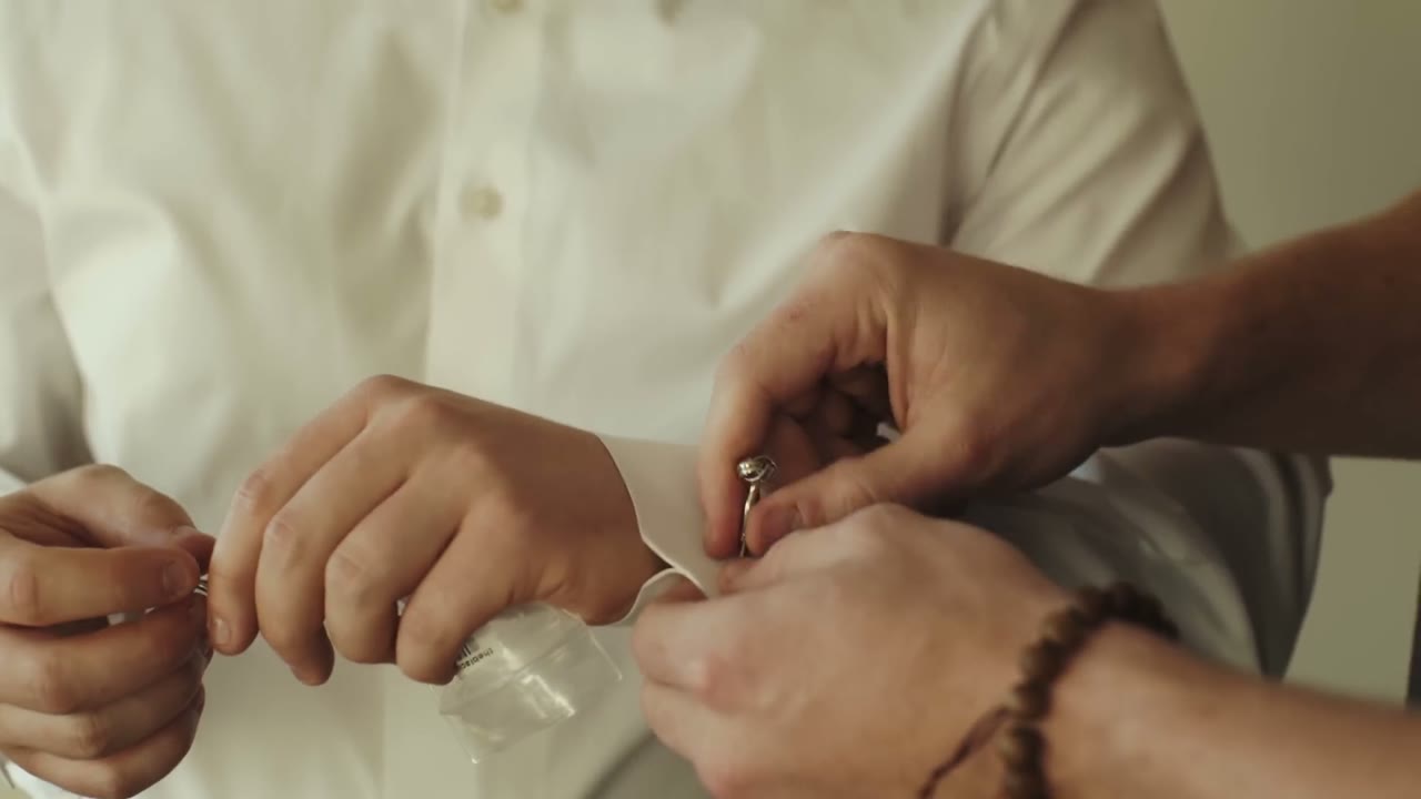 Close-up of hands fastening the groom's cufflinks over his white dress shirt