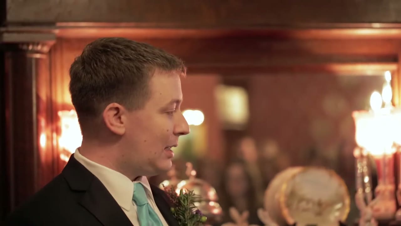 Groom in profile against ornate red damask wallpaper and lamplight, wearing a mint green tie