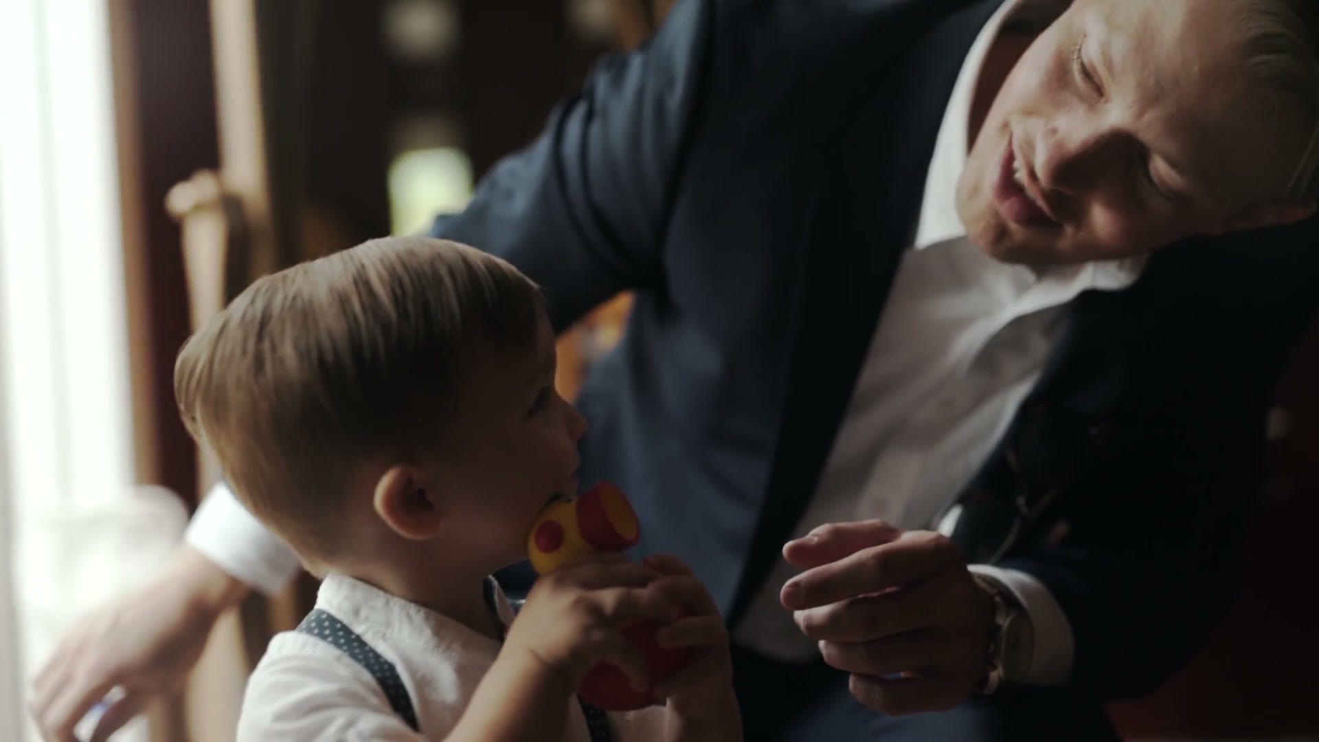 Groom crouching face to face with a toddler holding a toy in a tender moment