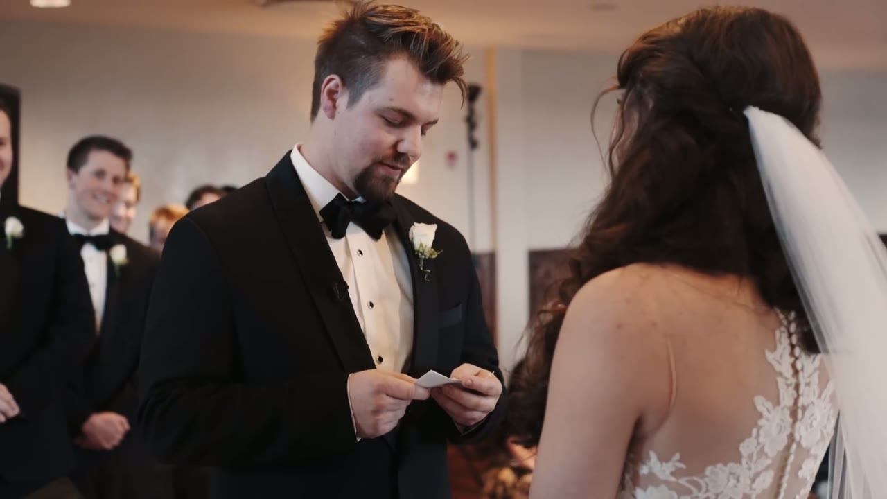 Groom reading his vows from a note card as the bride in a lace veil listens