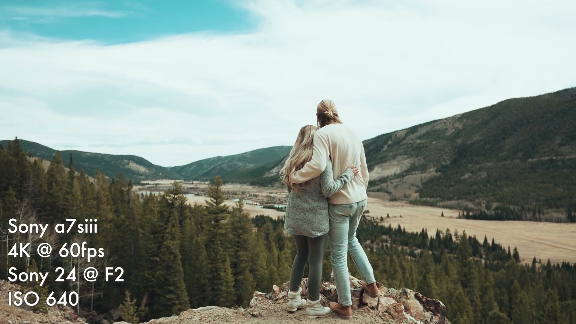 Holly and Luke standing arm in arm on a rocky outcropping looking out over a wide Colorado valley and forest
