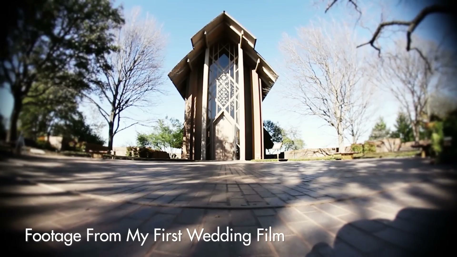 A wide fisheye shot of a modern chapel with a tall pointed roof, labelled Footage From My First Wedding Film