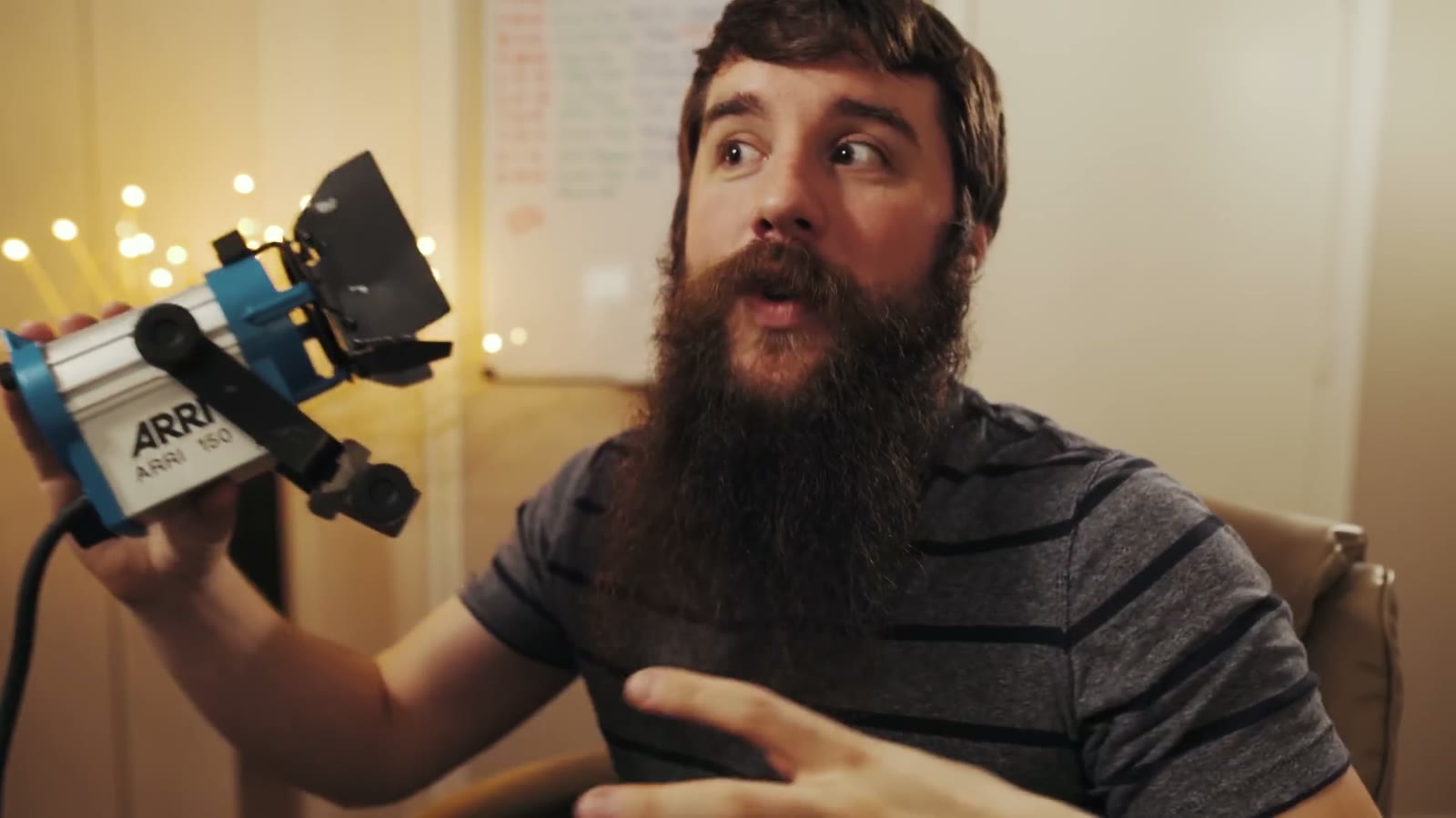 Matt holding an Arri 150 light fixture with a surprised wide-eyed expression, string lights behind him
