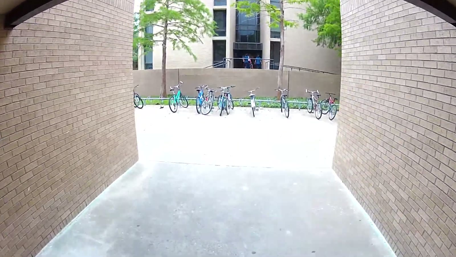 Fisheye view through a brick archway toward a row of parked bicycles and a campus building