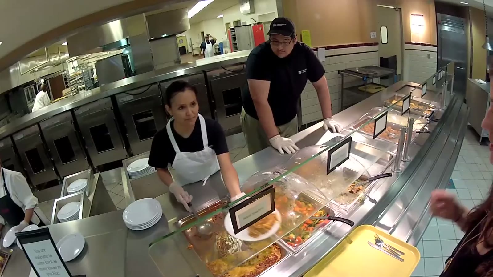 Two dining hall staff in Texas A&M polos serving food to a plate at the buffet line