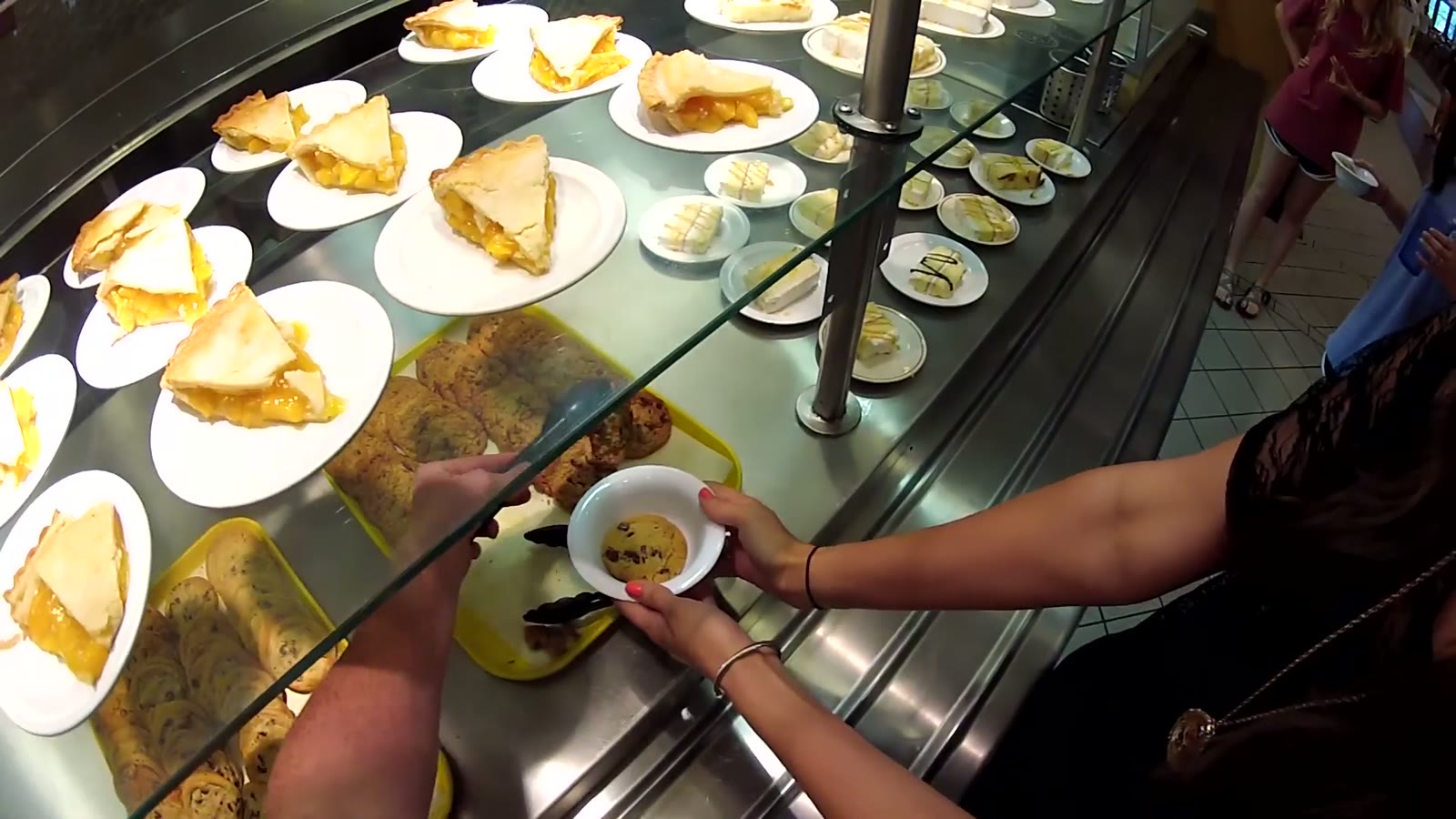 Overhead view of a dessert station with pie slices and cookies on plates, a hand reaching for a cookie