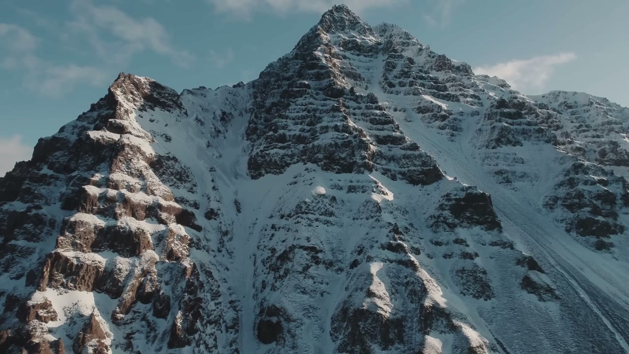 Snow-capped Icelandic mountain peak against a pale blue sky with scattered clouds