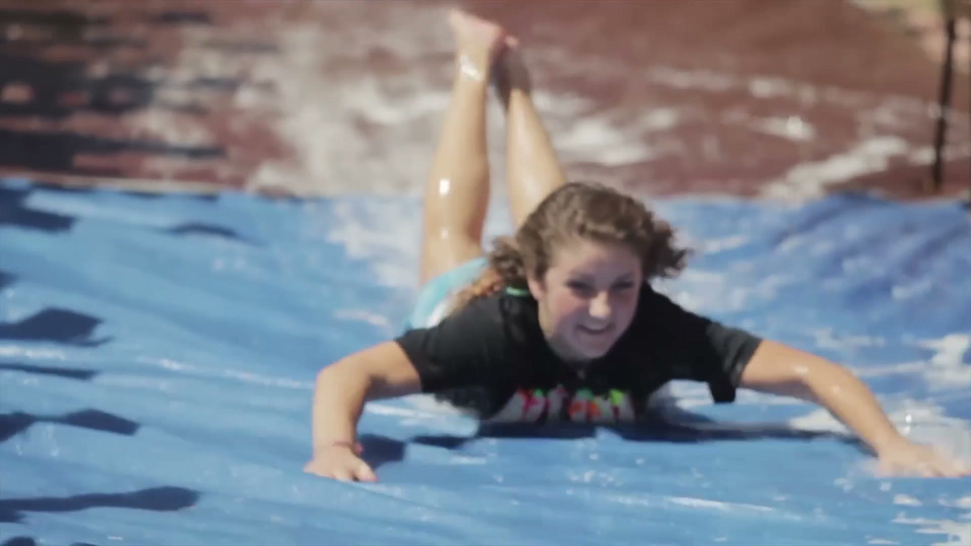 A student sliding face first down a long blue plastic sheet covered in water and soap