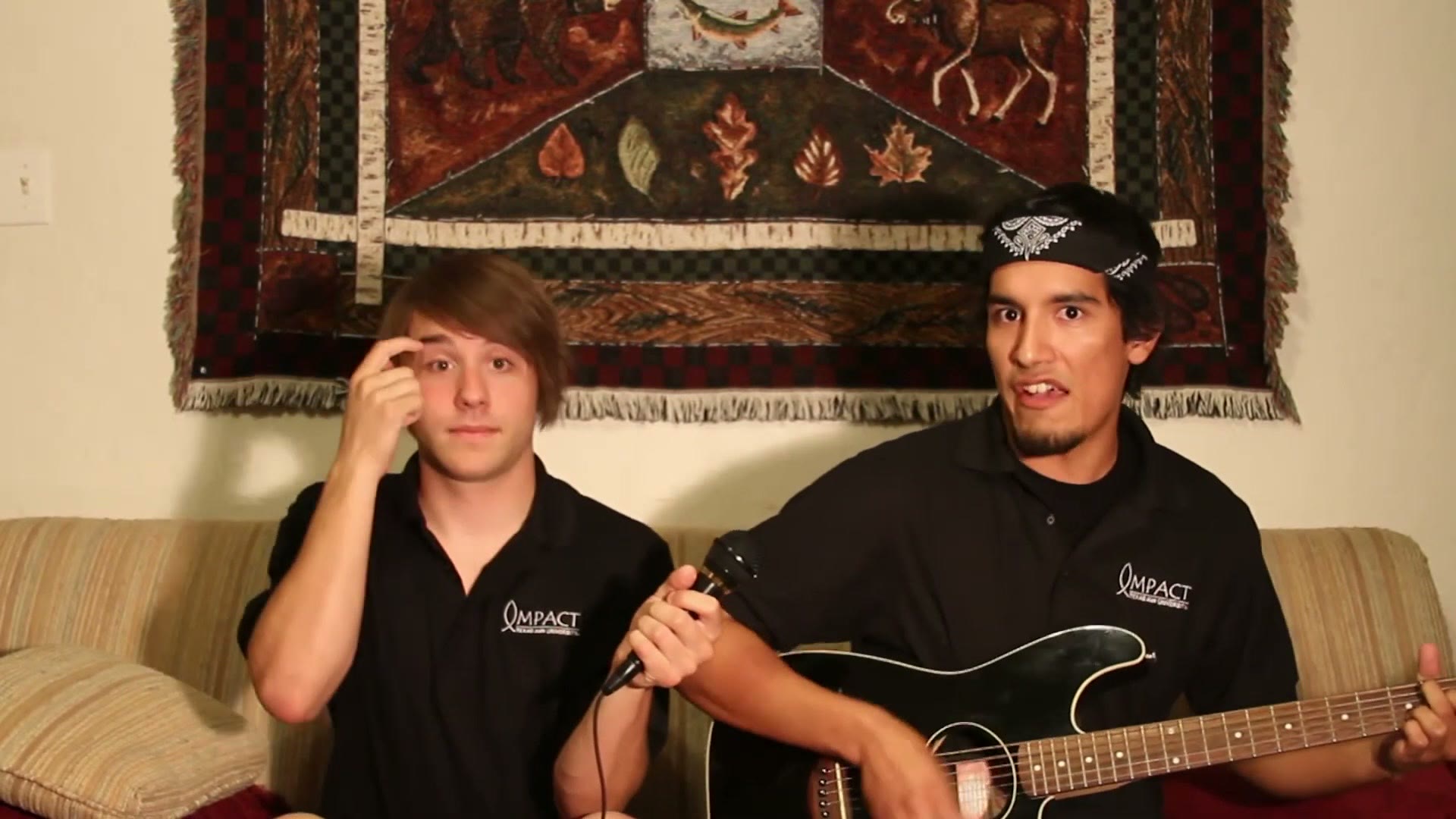 The two students on the couch, one playing an electric guitar and the other holding a microphone