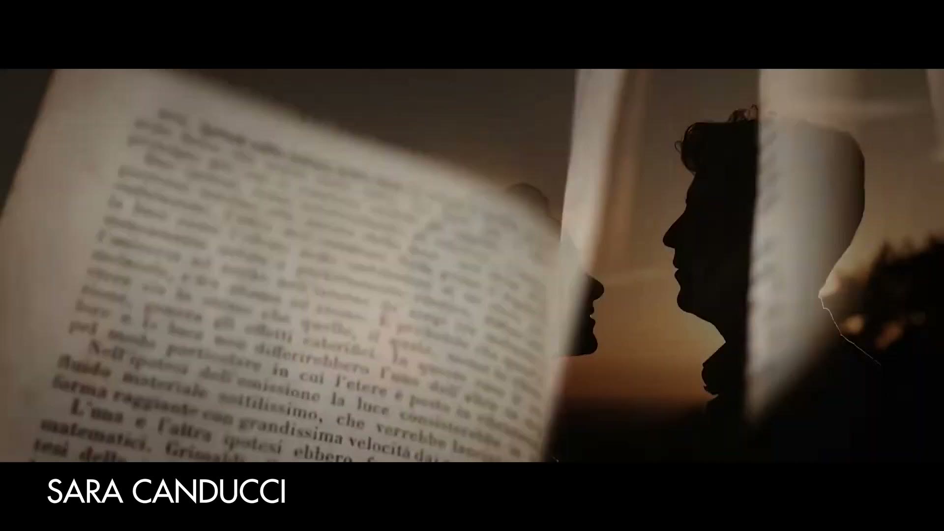 A wedding film frame of an open antique book in the foreground and a bride and groom in silhouette behind a sheer curtain at sunset, credited on screen to Sara Canducci