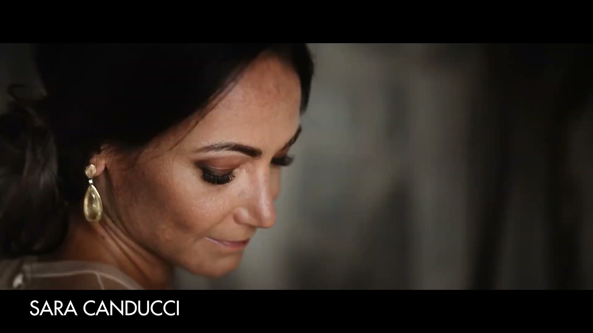 A close up of a bride looking down, wearing a gold drop earring, credited on screen to Sara Canducci