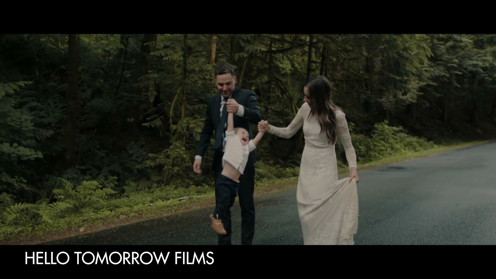 A groom and bride walking down a forest road swinging their young son between them by the hands, credited on screen to Hello Tomorrow Films
