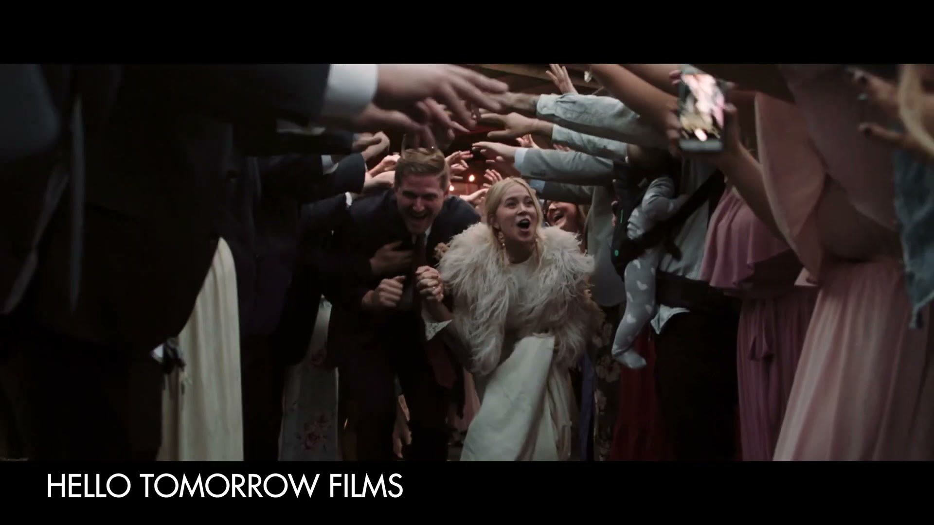 A bride and groom running out through a tunnel of raised hands and cheering guests, credited on screen to Hello Tomorrow Films