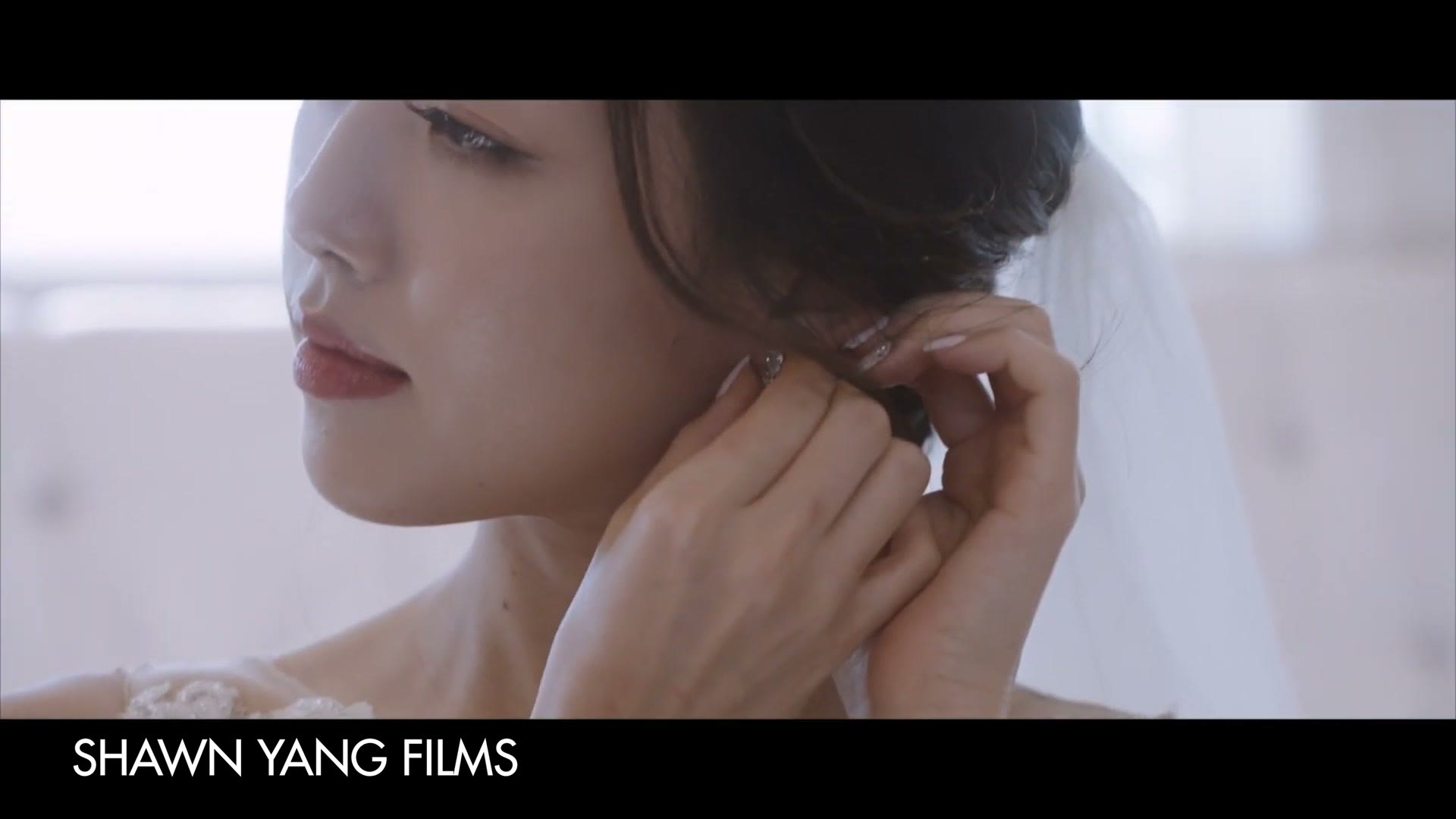 A close up of a bride in a veil fastening an earring, credited on screen to Shawn Yang Films