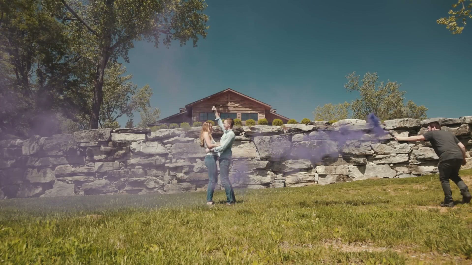 A wide 360 frame of a couple spinning a selfie stick overhead in purple smoke, with Matt visible at the right of frame holding the smoke canister