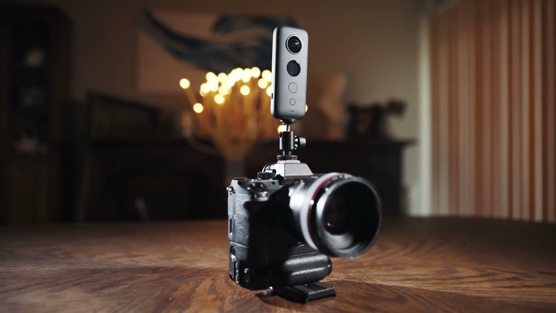 An Insta360 ONE X mounted upright on the hot shoe of a Sony mirrorless camera with a battery grip, sitting on a wooden table