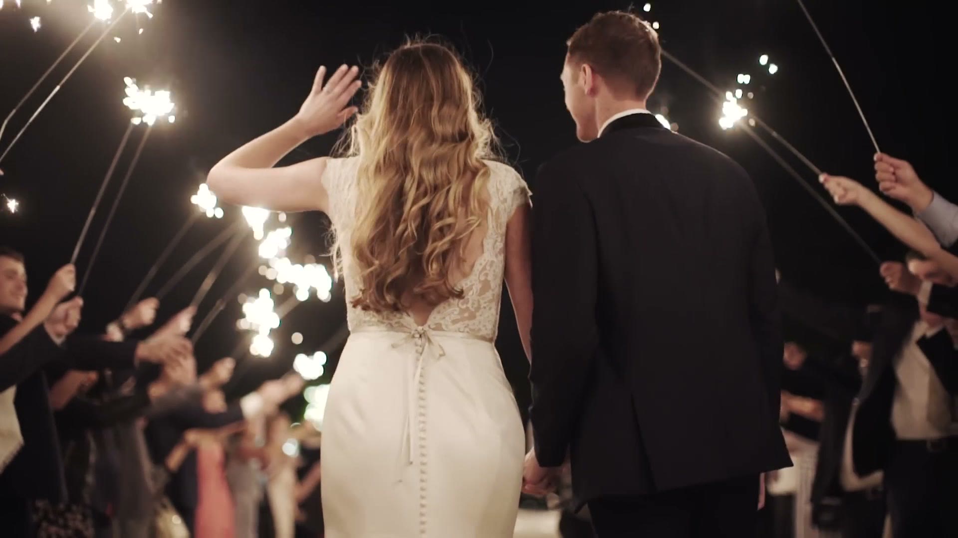 A clean, sharp shot of a bride and groom walking through a sparkler tunnel at night, filmed on a Sony a7S II